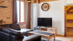 Una sala de estar moderna con una pared de piedra, techo de madera, un sofá de cuero, una mesa de centro de madera, un televisor y un reloj.