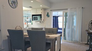 Een eethoek met een tafel en stoelen, een keuken op de achtergrond en een glazen schuifdeur naar een balkon.