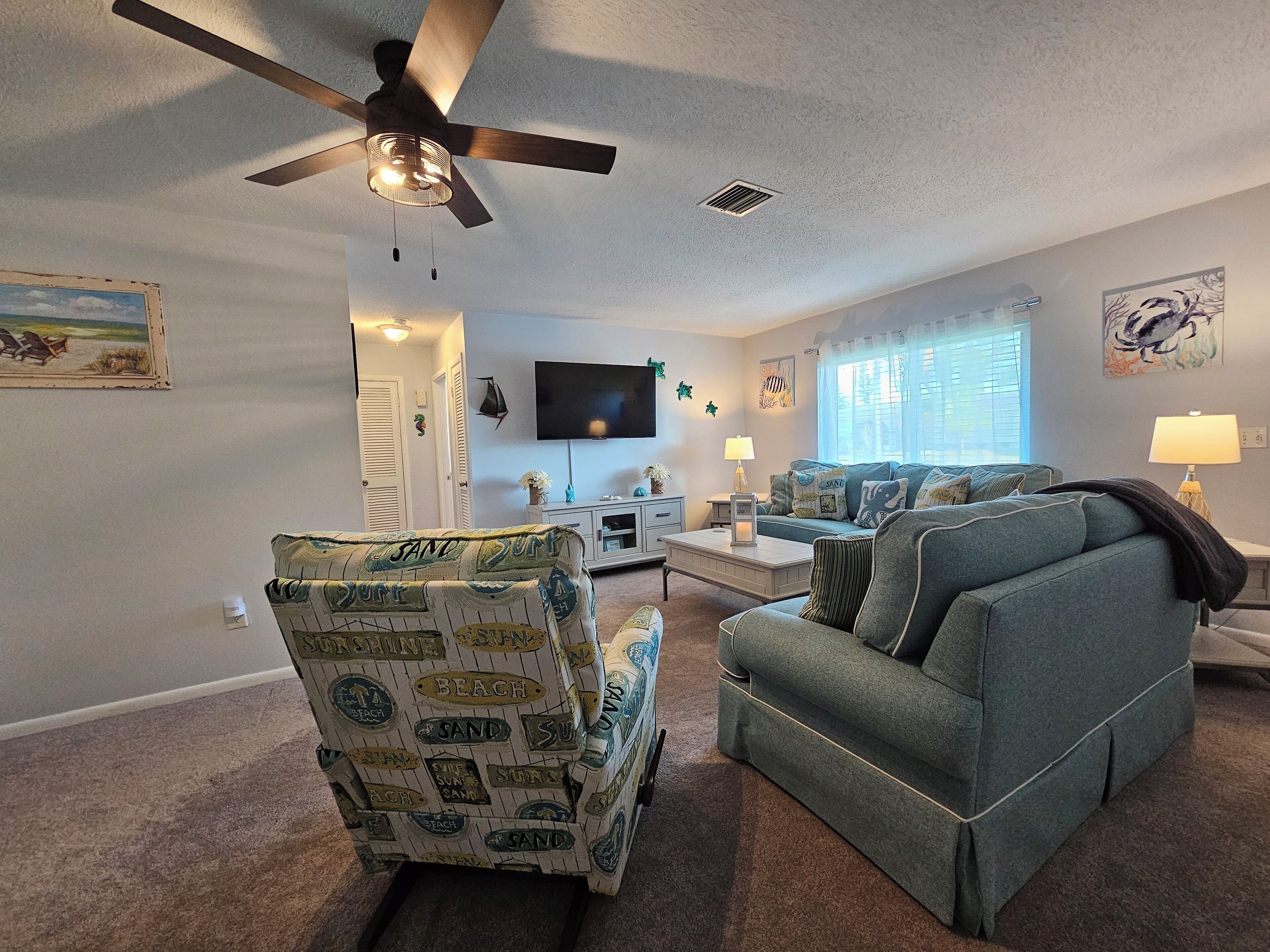A living room with a ceiling fan, a TV mounted on the wall, a sofa, a chair, and a coffee table.