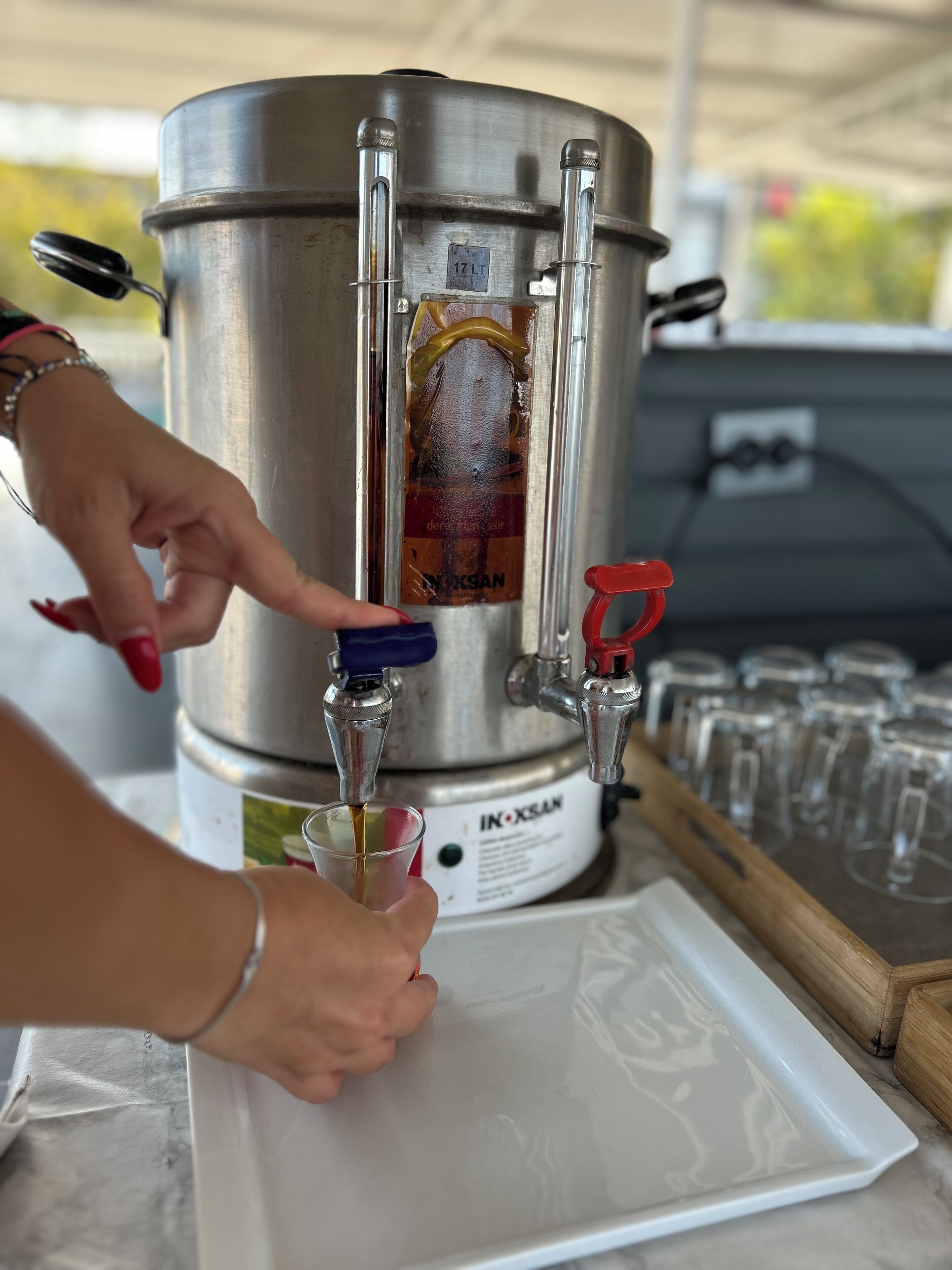 Un distributeur de boissons en acier inoxydable, doté de deux robinets, portant une étiquette indiquant « IN-XSAK », et une personne versant une boisson dans un verre.