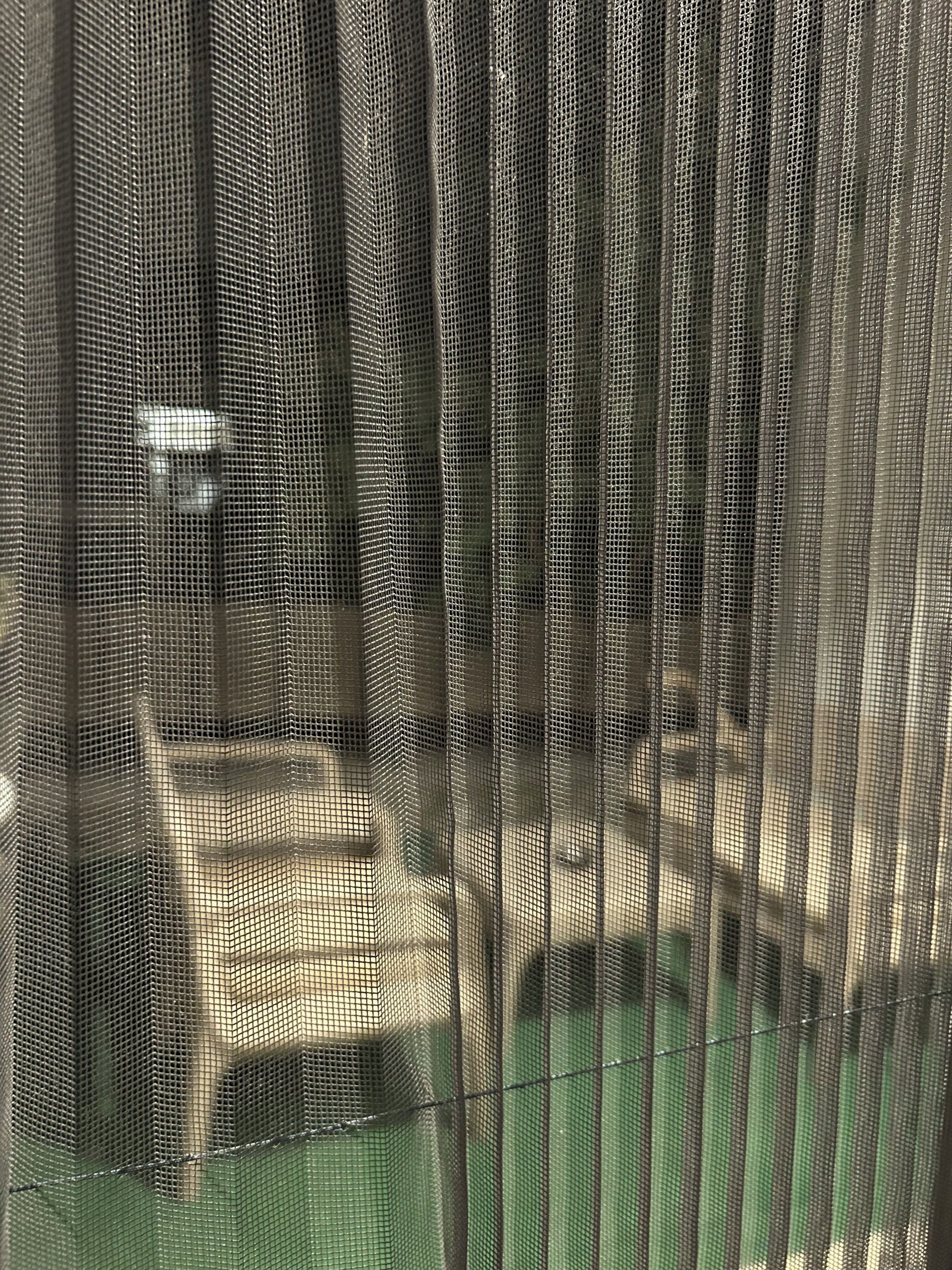 A close-up of a mesh fence with a grid pattern, likely part of a larger structure.