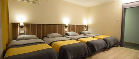 A hotel room with four beds arranged in a row, each with a headboard and bedside lamps.
