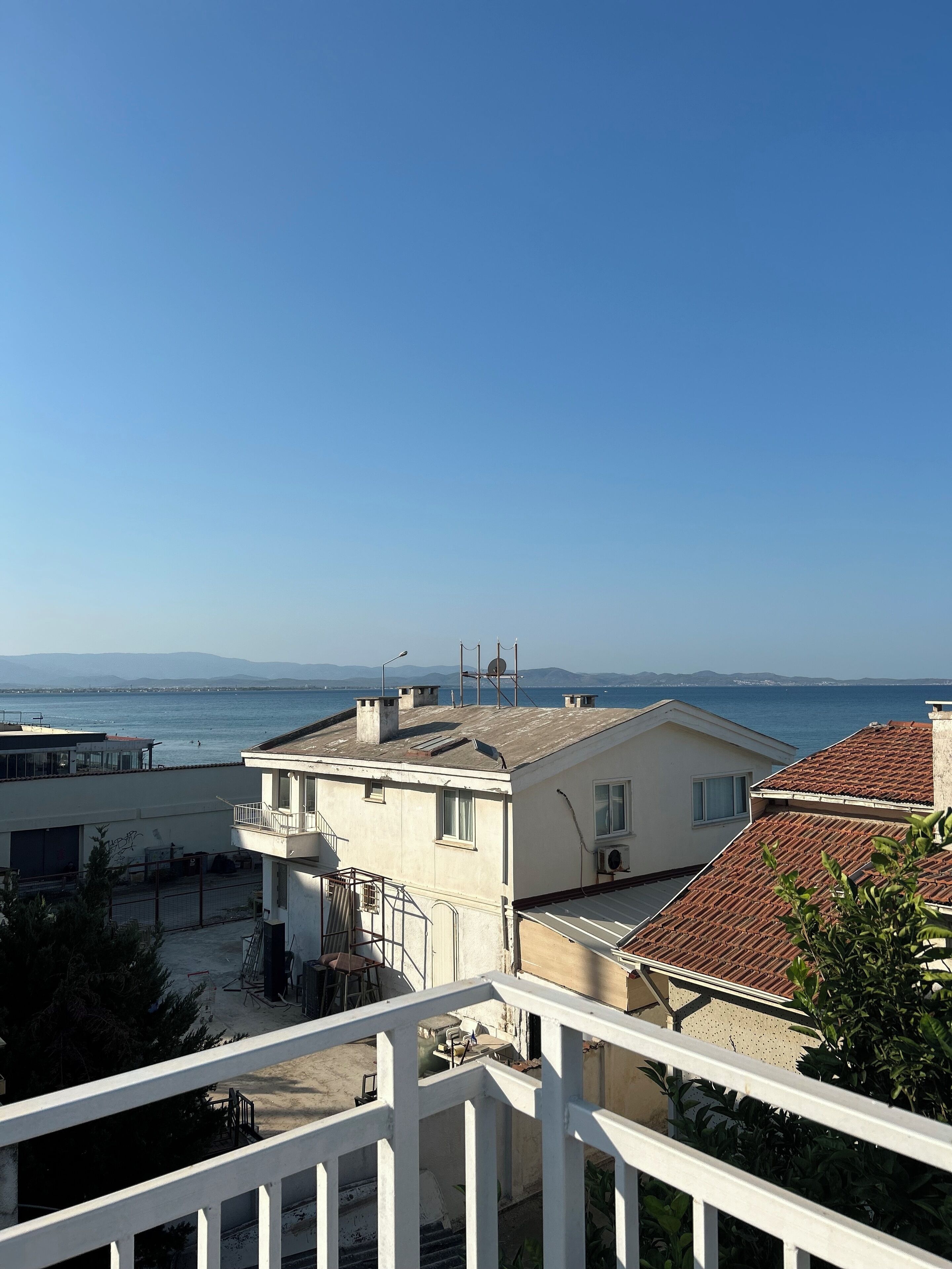 A residential area with a view of the sea, featuring buildings with tiled roofs and a balcony railing.