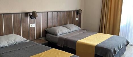 A hotel room with two beds, a wooden headboard, a wall-mounted air conditioner, and a window with curtains.