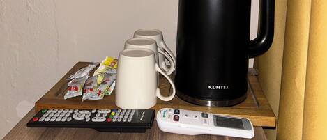 A wooden table with a black kettle, white mugs, and a remote control.