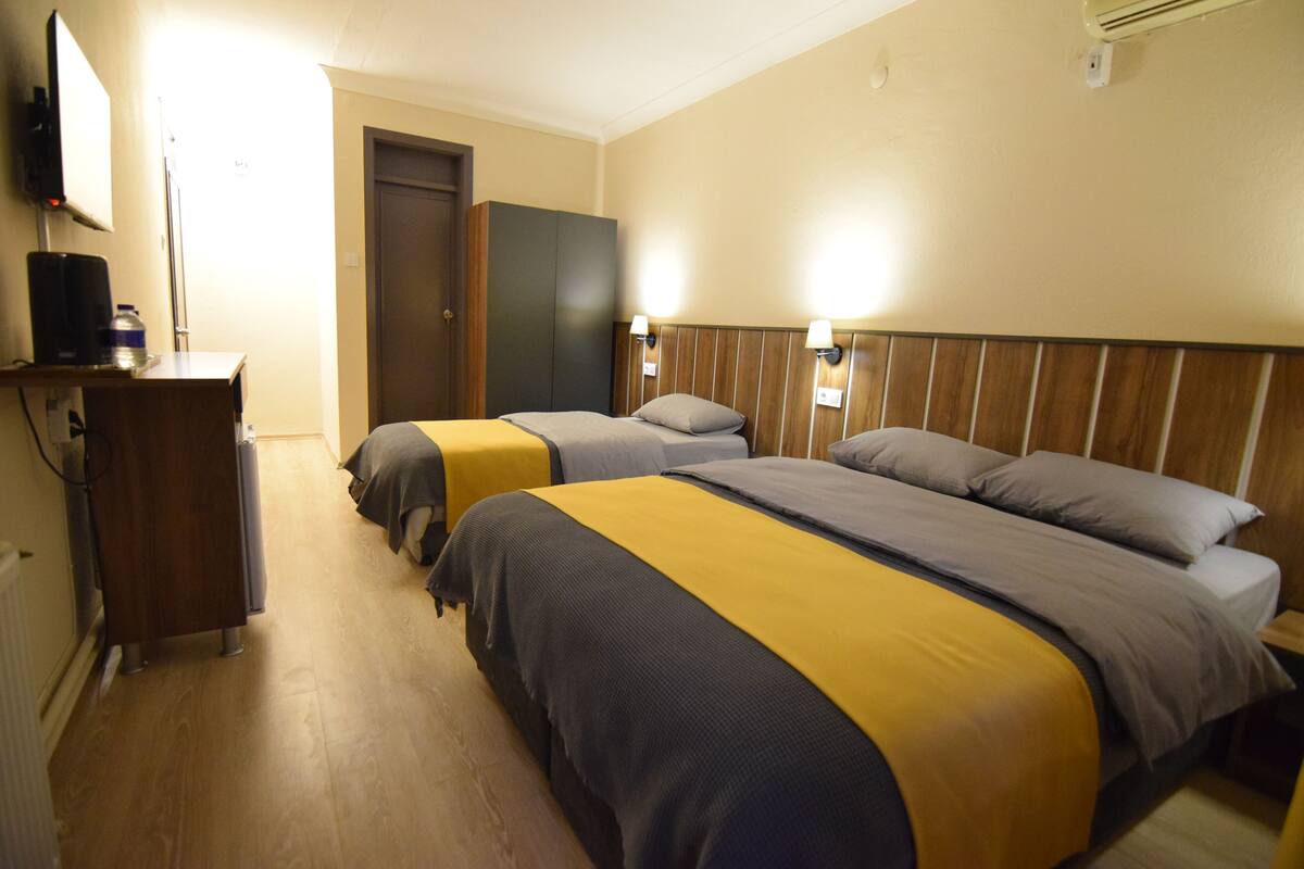 A hotel room with two beds, a wooden headboard, a desk with a computer, and a door.
