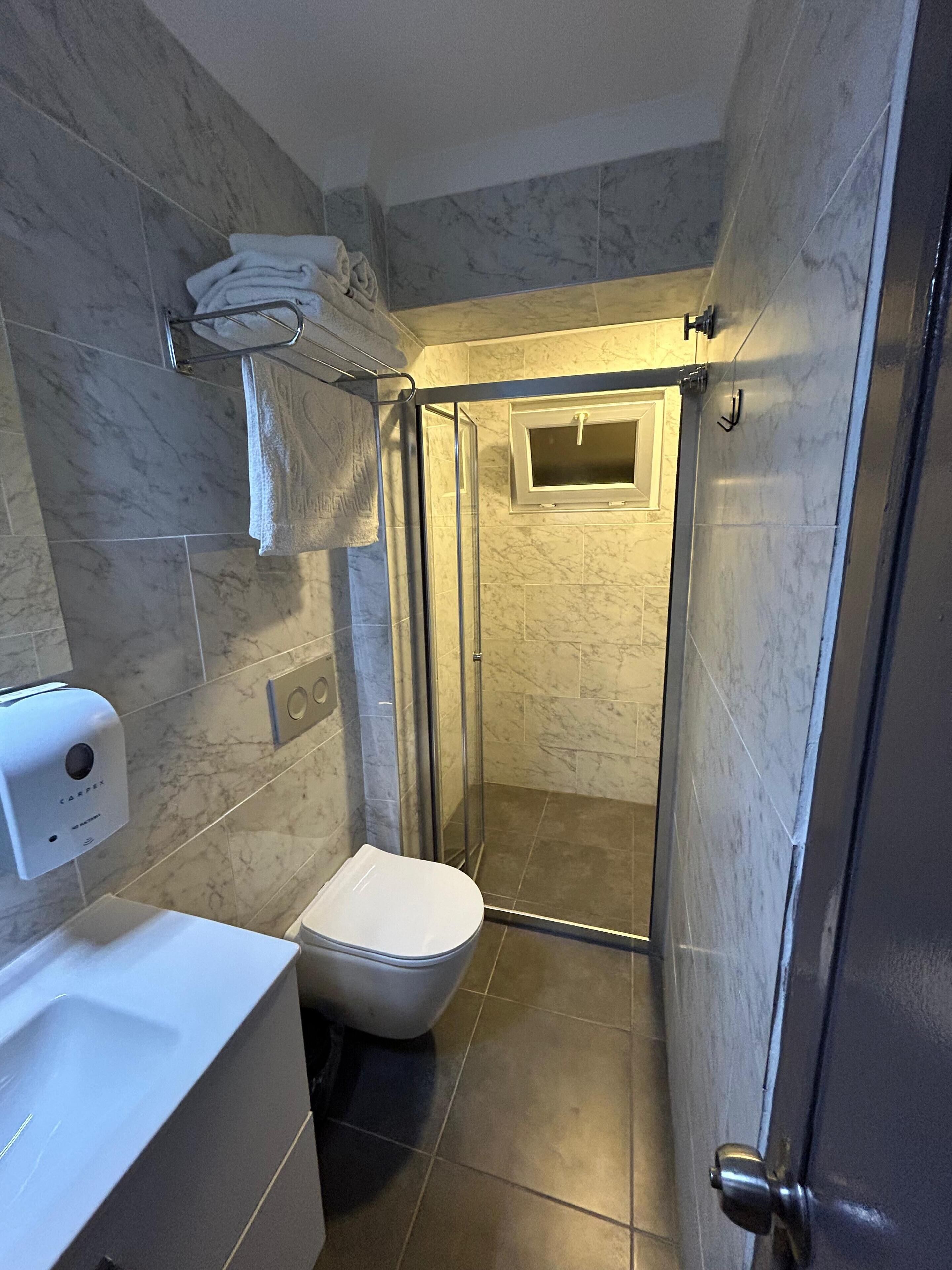 A compact bathroom with a toilet, a shower stall, and a towel rack.