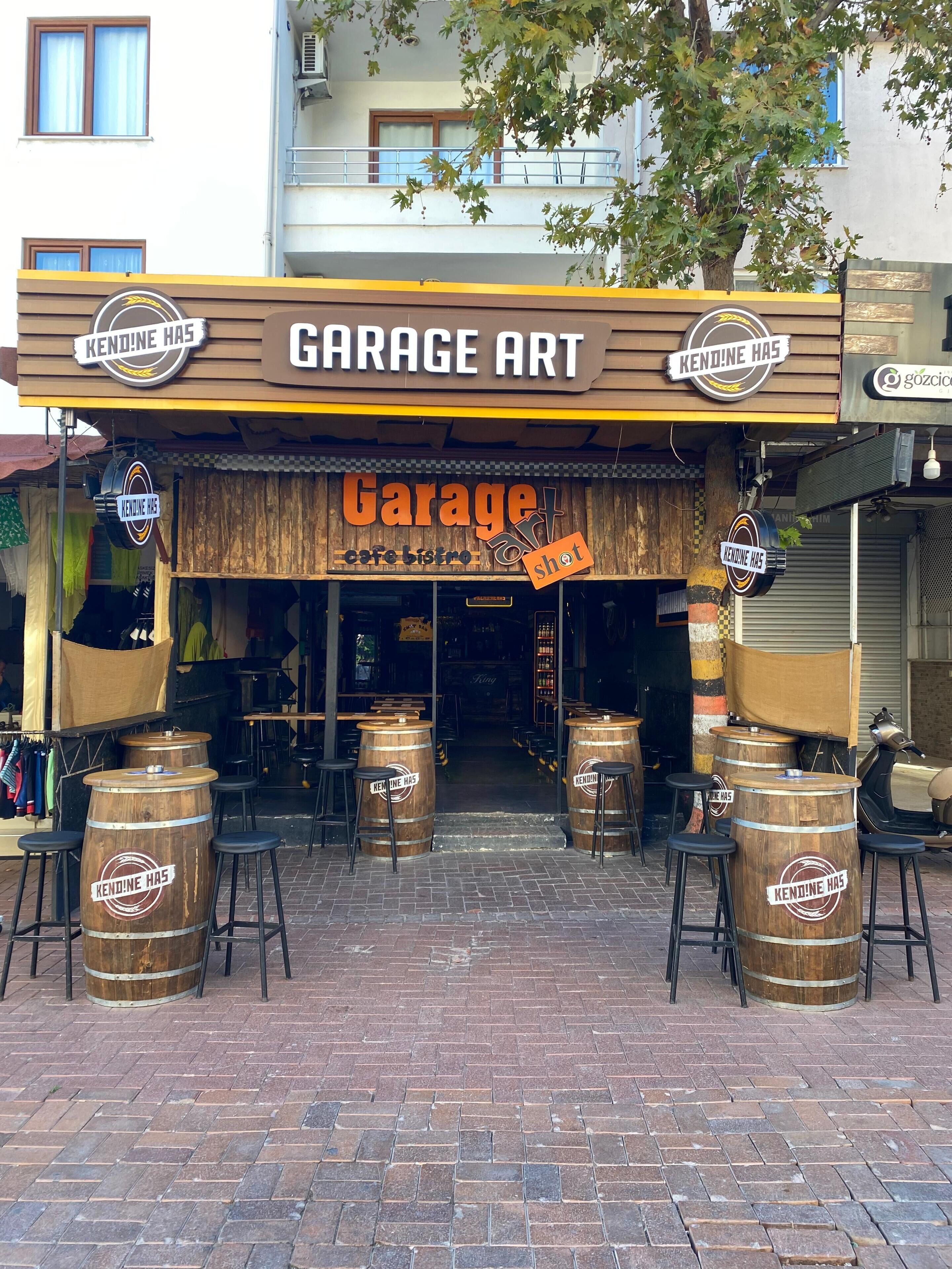 Une boutique appelée « Garage Art », avec une façade rustique en bois, des tabourets de bar et des tonneaux en bois.