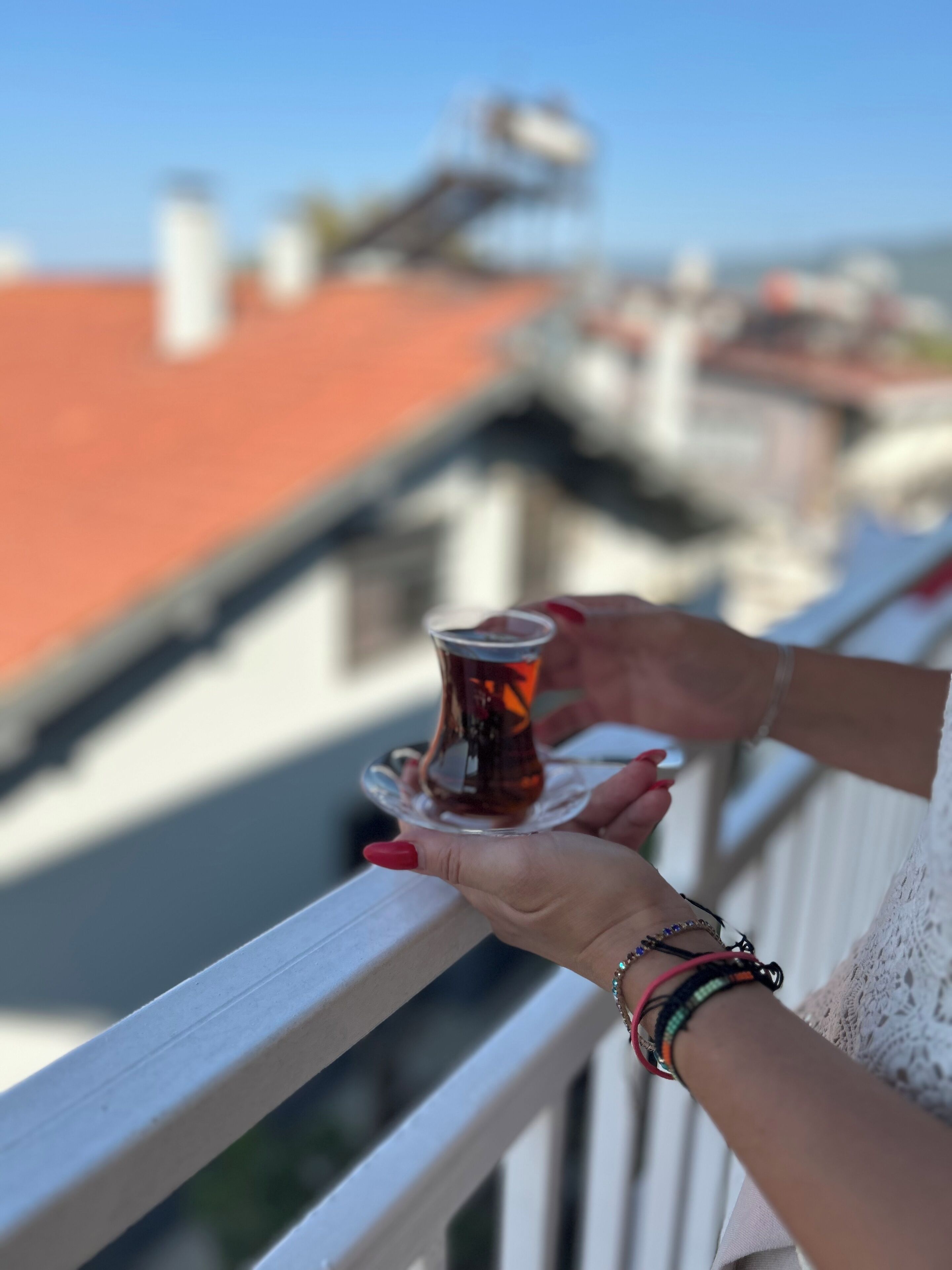 Eine Person hält auf dem Balkon eine Teetasse, im Hintergrund sind Gebäude und ein Fluss zu sehen.