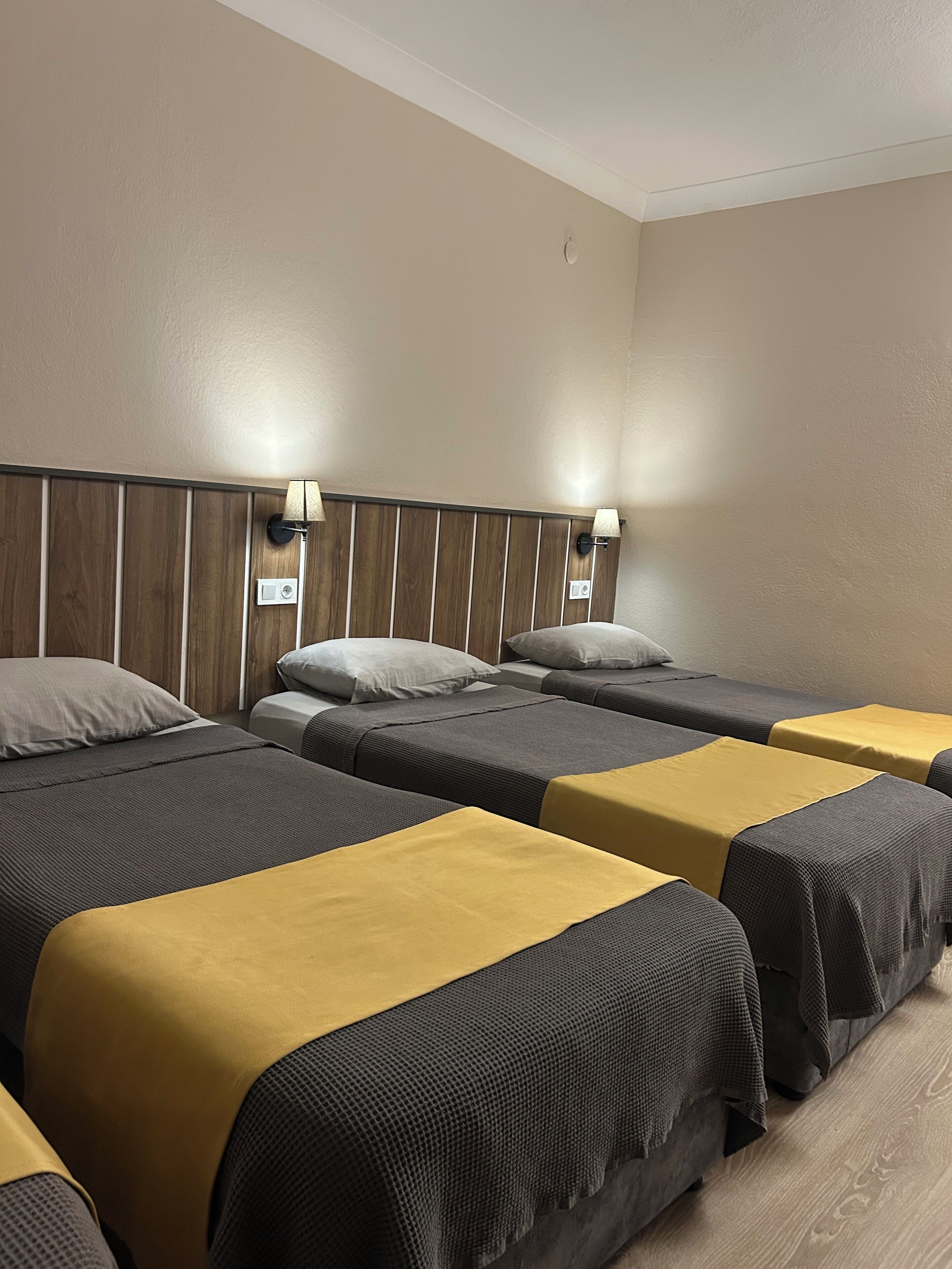 A hotel room with four single beds arranged in a row, each with a headboard and a bedside lamp.