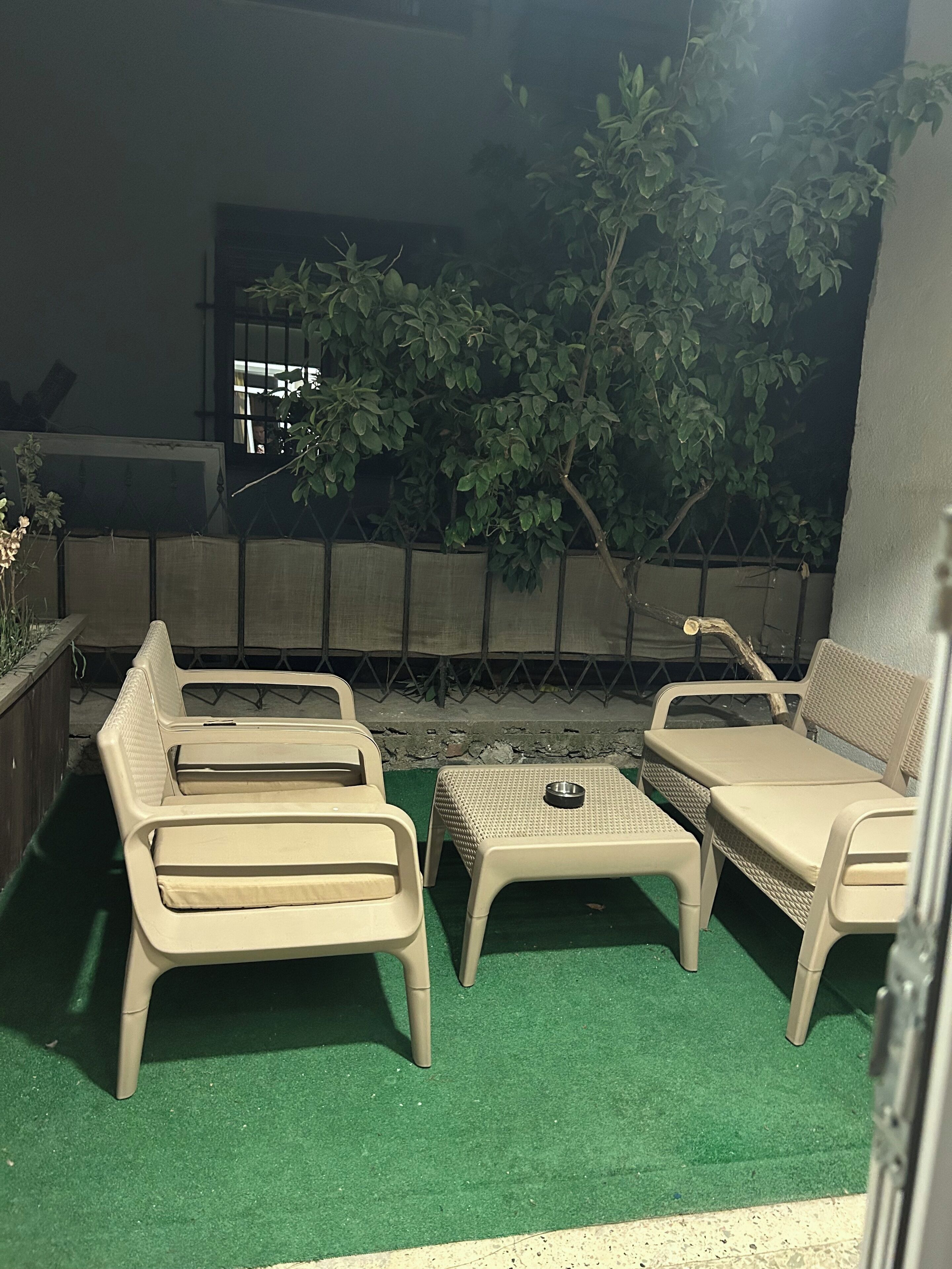 An outdoor seating area with plastic chairs and a small table, surrounded by a green artificial turf.