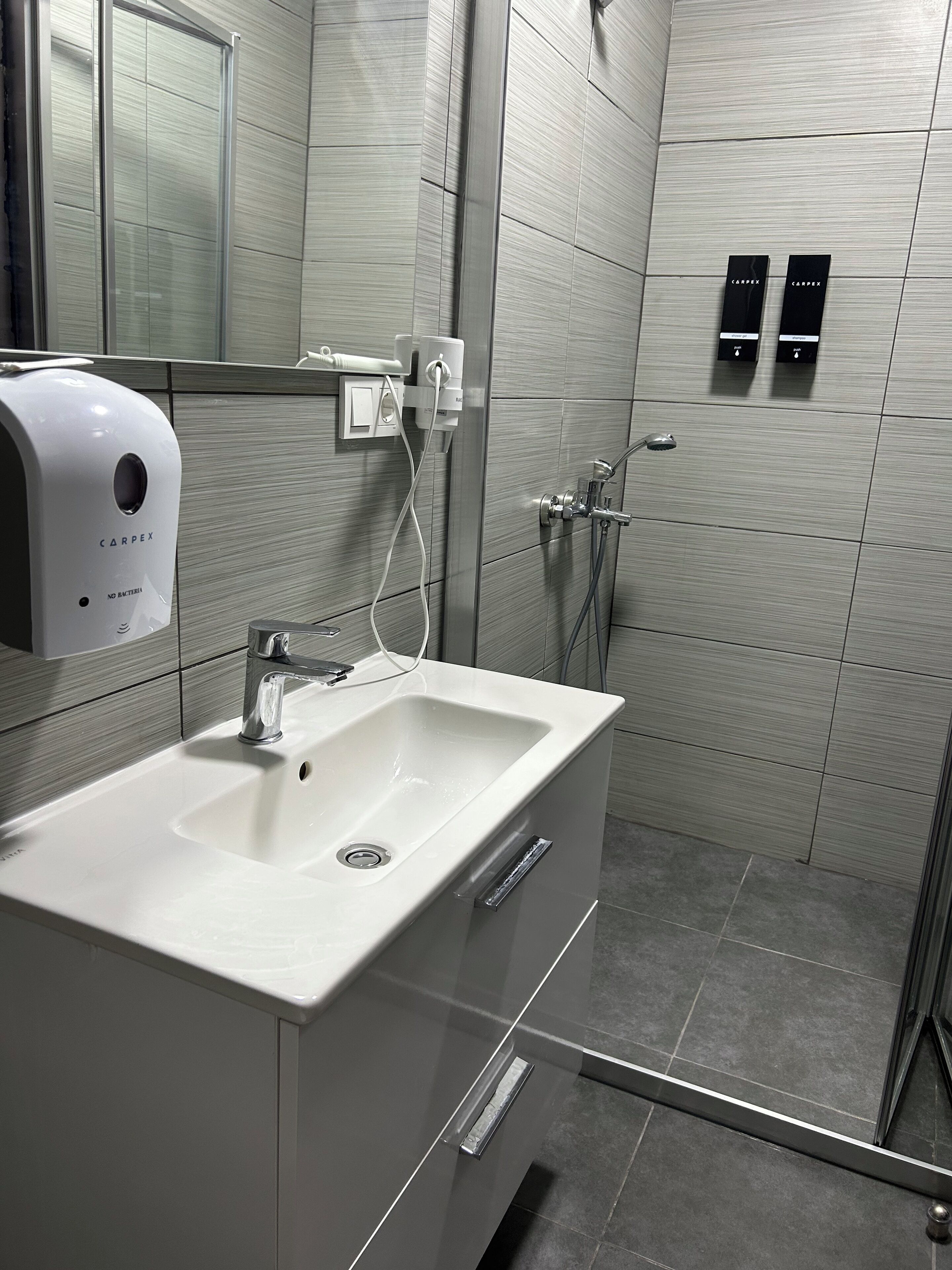 Un baño moderno con un lavamanos blanco, un secador de manos y una zona de ducha.