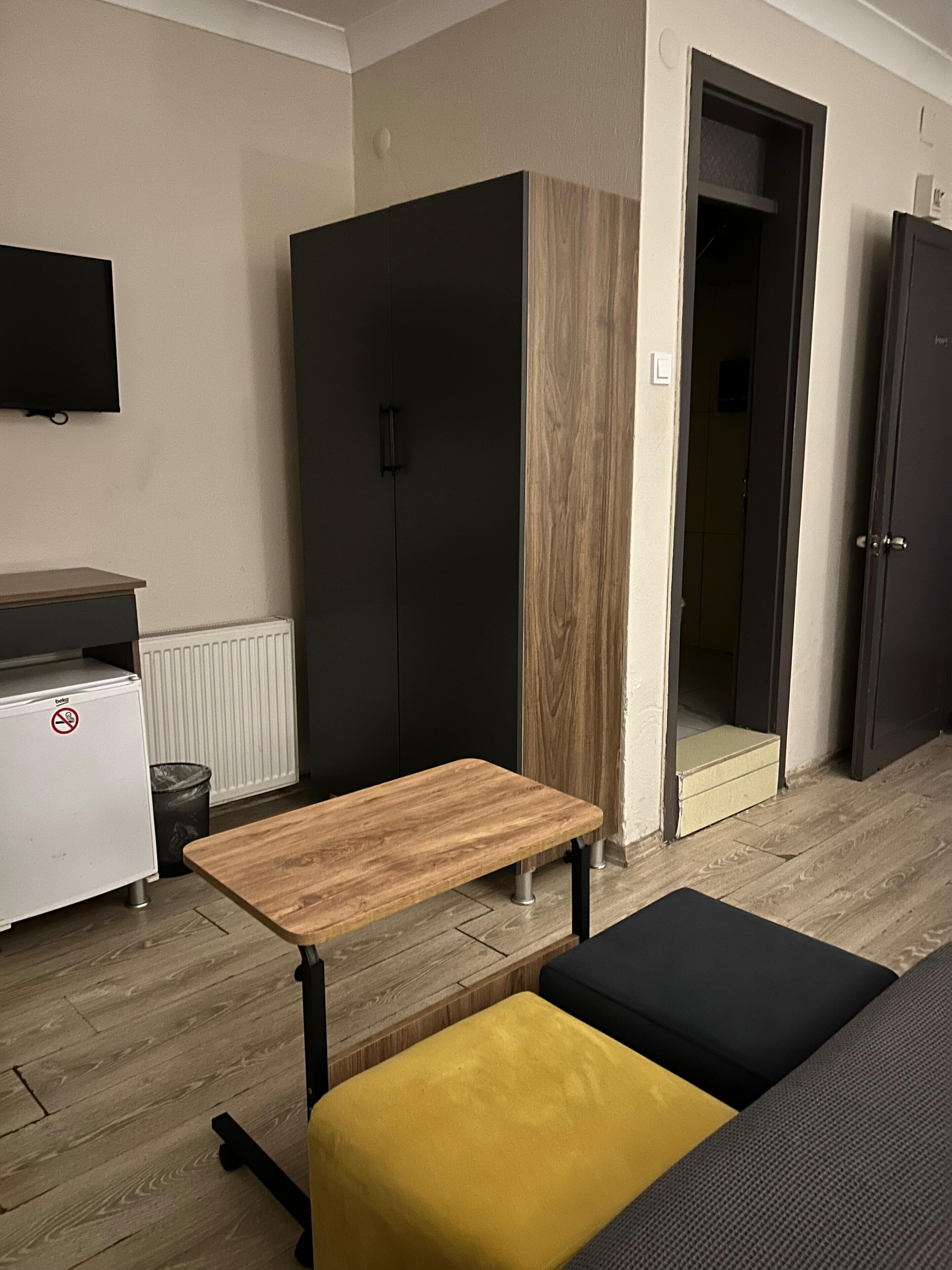 A compact room with a wooden table, a sofa, a bench, a kitchenette, and a wardrobe.