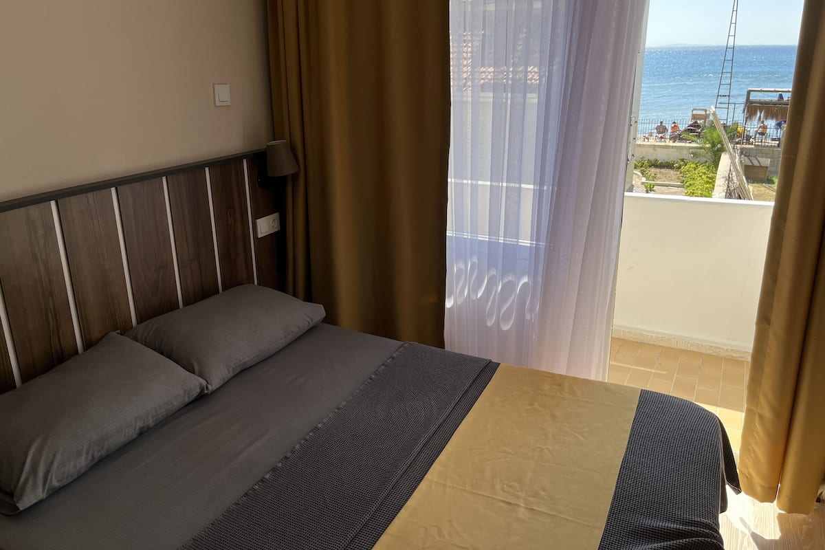 A bedroom with a bed, curtains, and a view of the sea.