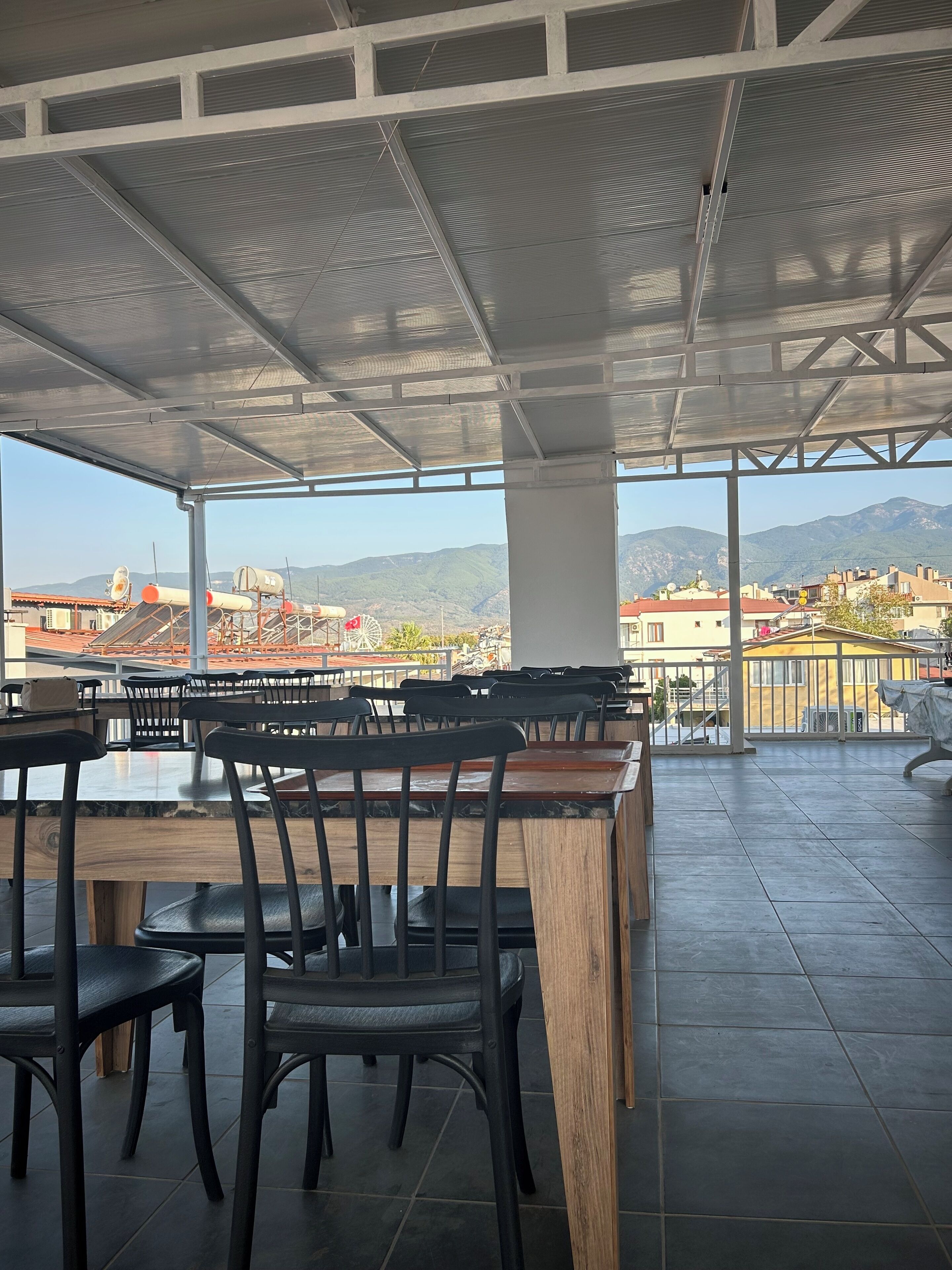 An outdoor seating area with tables and chairs, a view of mountains, and a cityscape in the background.