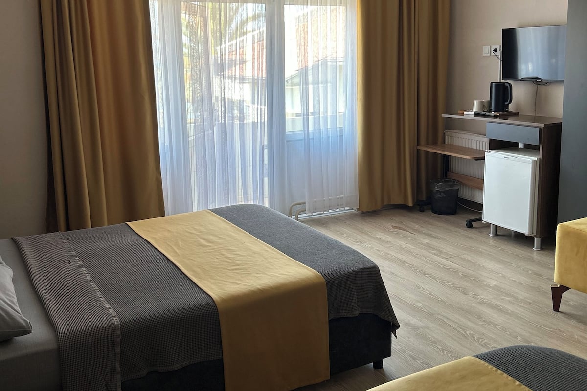 A hotel room with two beds, a desk with a TV, and a window with curtains.