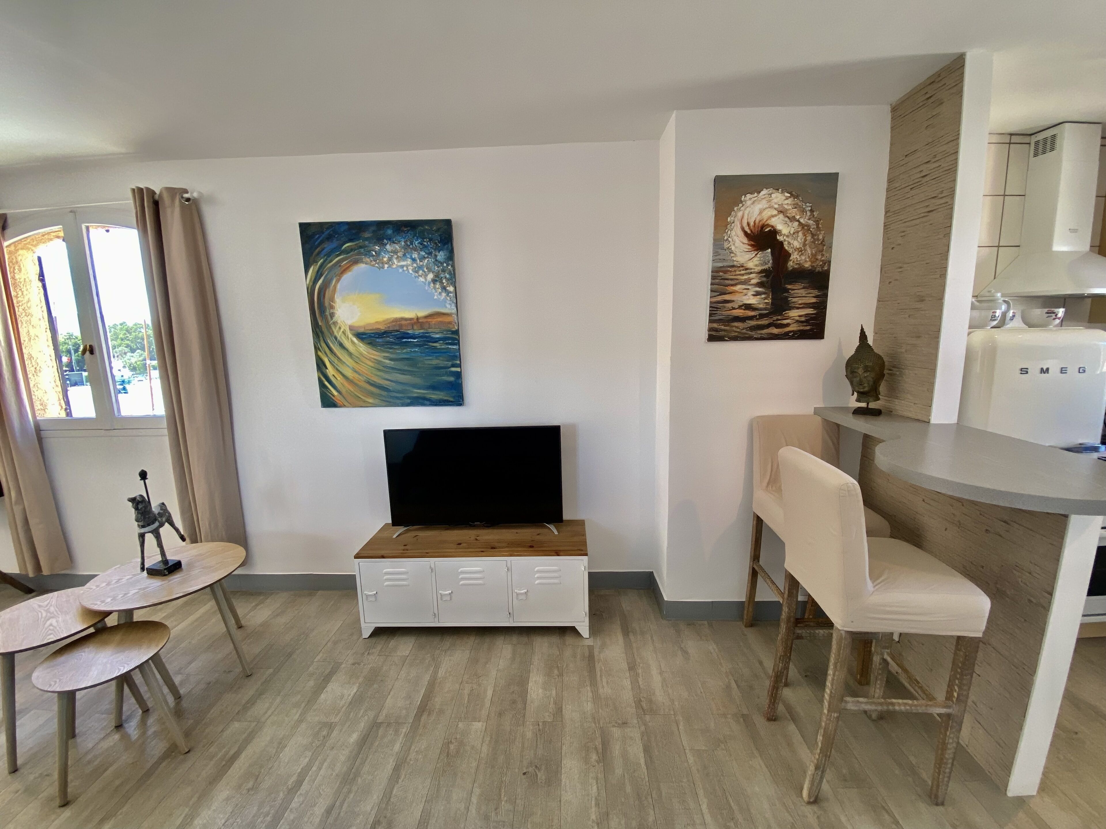 A modern living room with a flat-screen TV, a dining area with a bar counter, and two paintings on the walls.