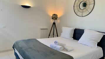 Een keurig opgemaakt bed met wit en grijs beddengoed, een ronde wandklok en een vloerlamp.