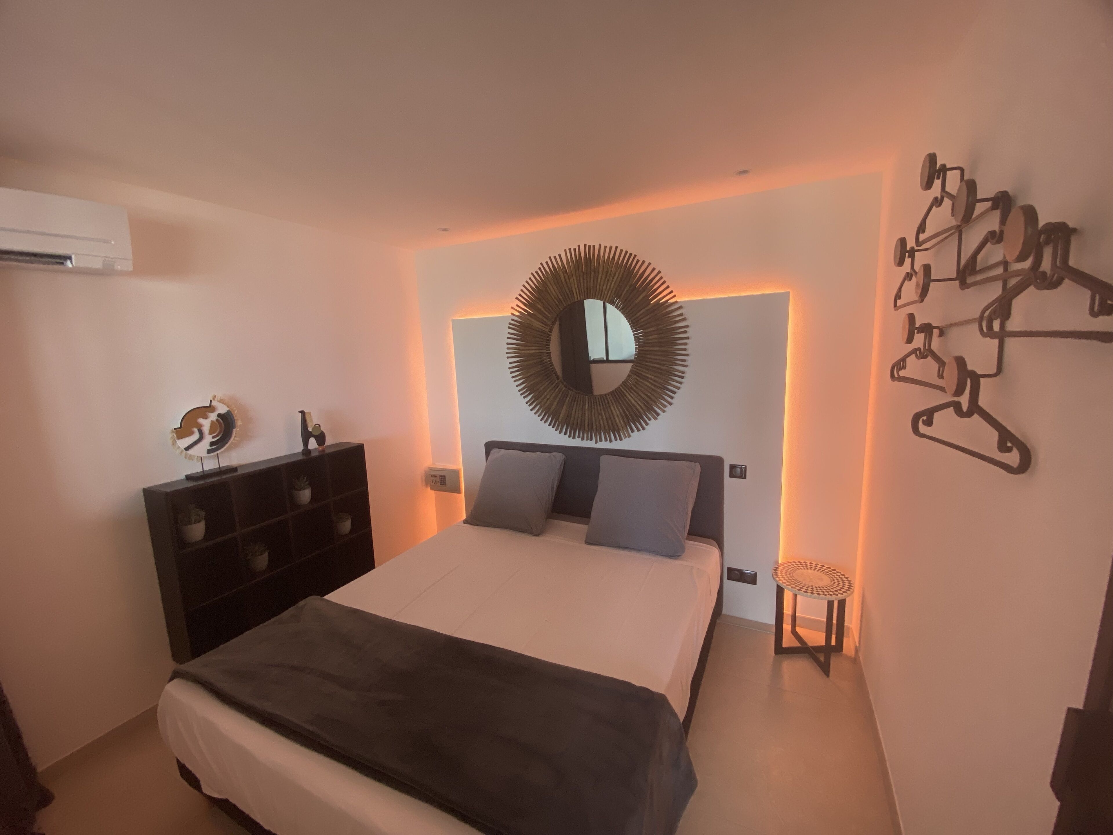 A modern bedroom with a bed, dresser, and wall-mounted mirror.