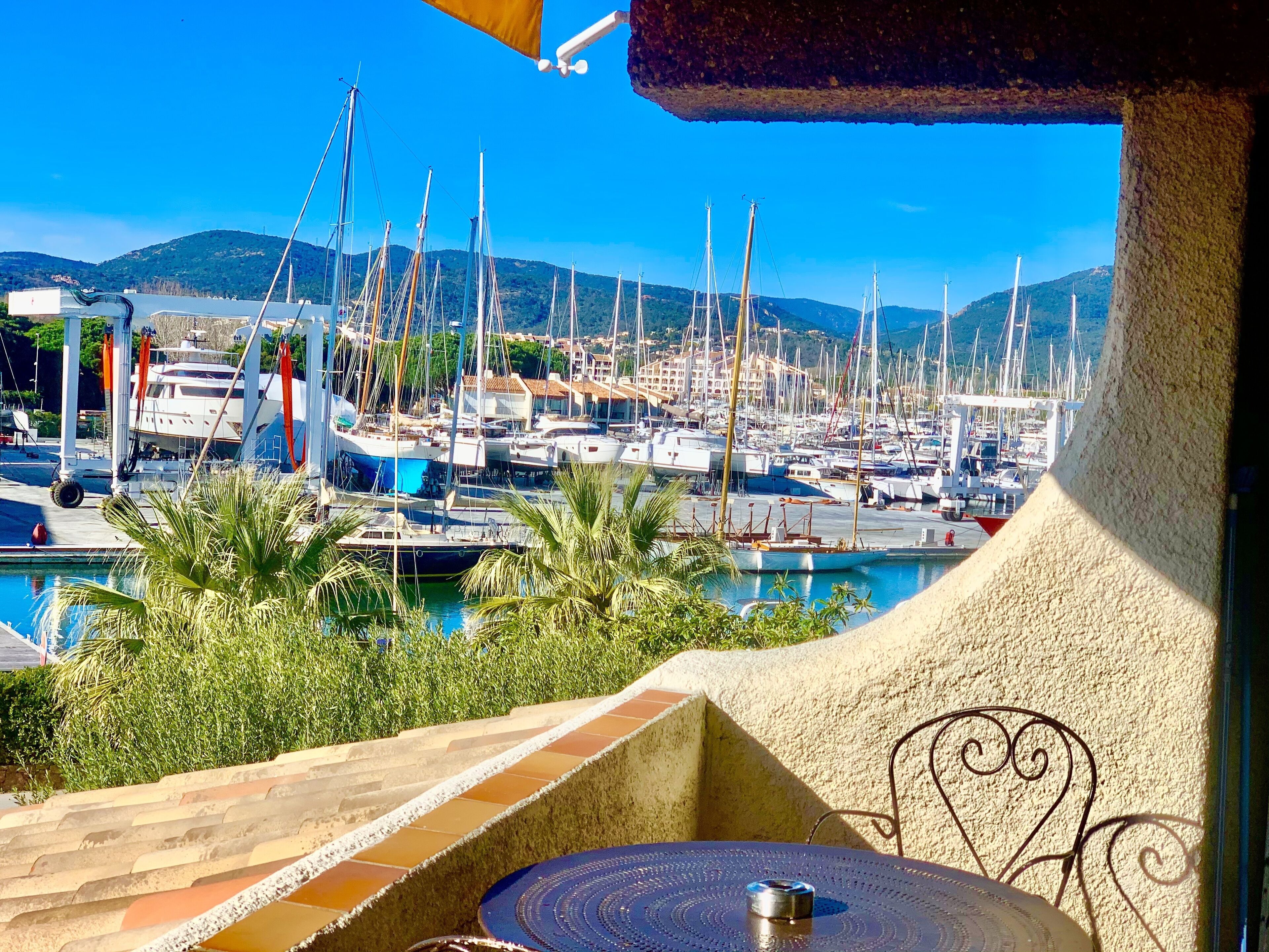 Un port de plaisance où sont amarrés de nombreux bateaux, une piscine et une vue sur des collines en arrière-plan.