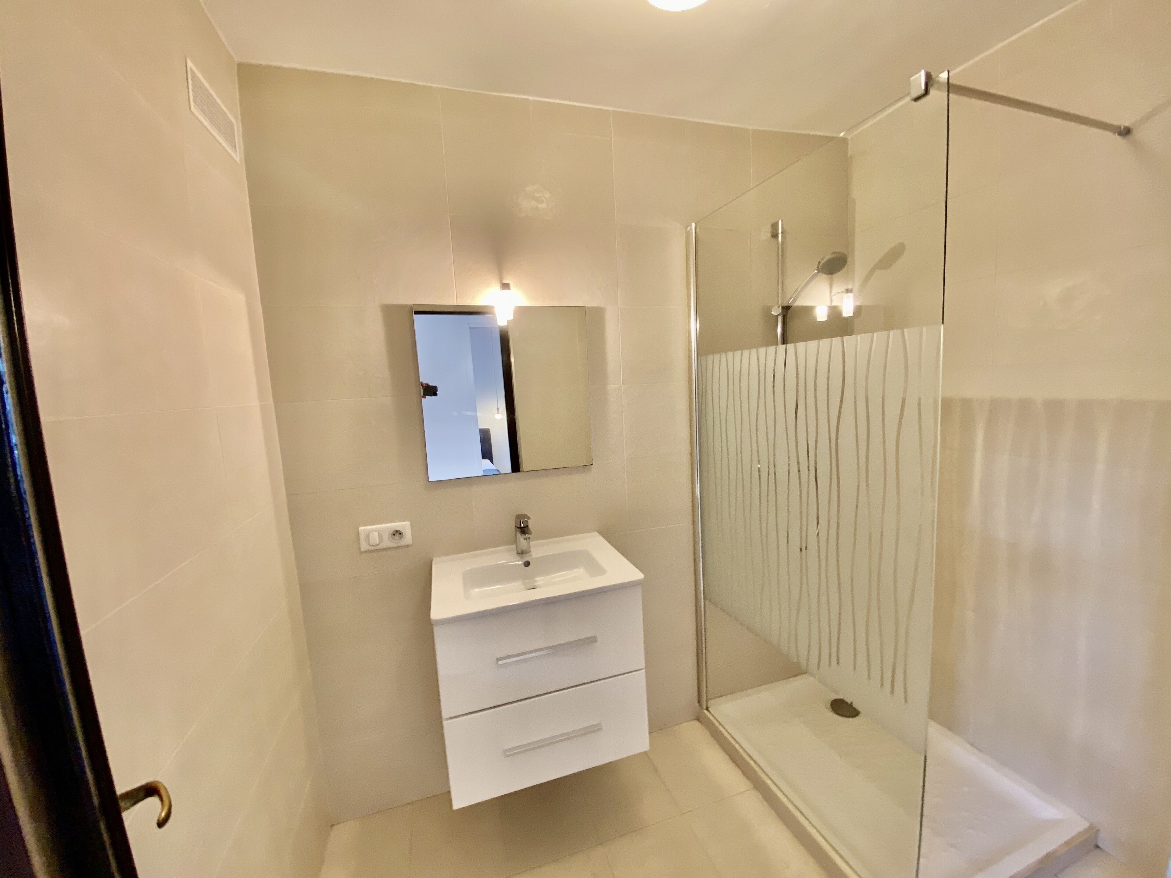 Une salle de bain moderne avec une douche à l’italienne en verre, un lavabo blanc et un miroir au-dessus.