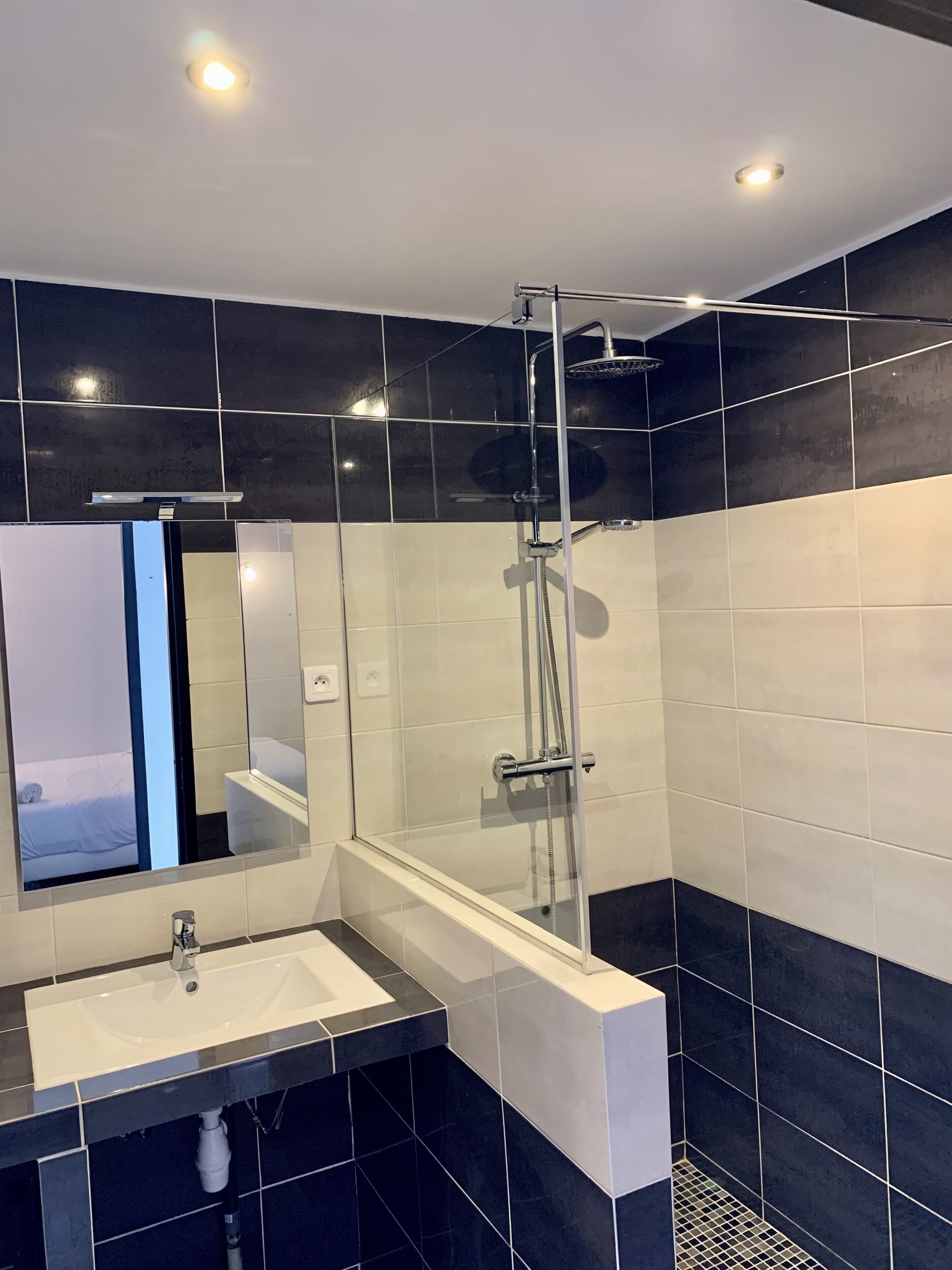 Un baño moderno con ducha de vidrio, lavamanos blanco y un espejo grande.