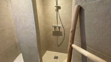 Un espace douche doté d’une barre d’appui en bois, de murs carrelés et d’un drain au sol.