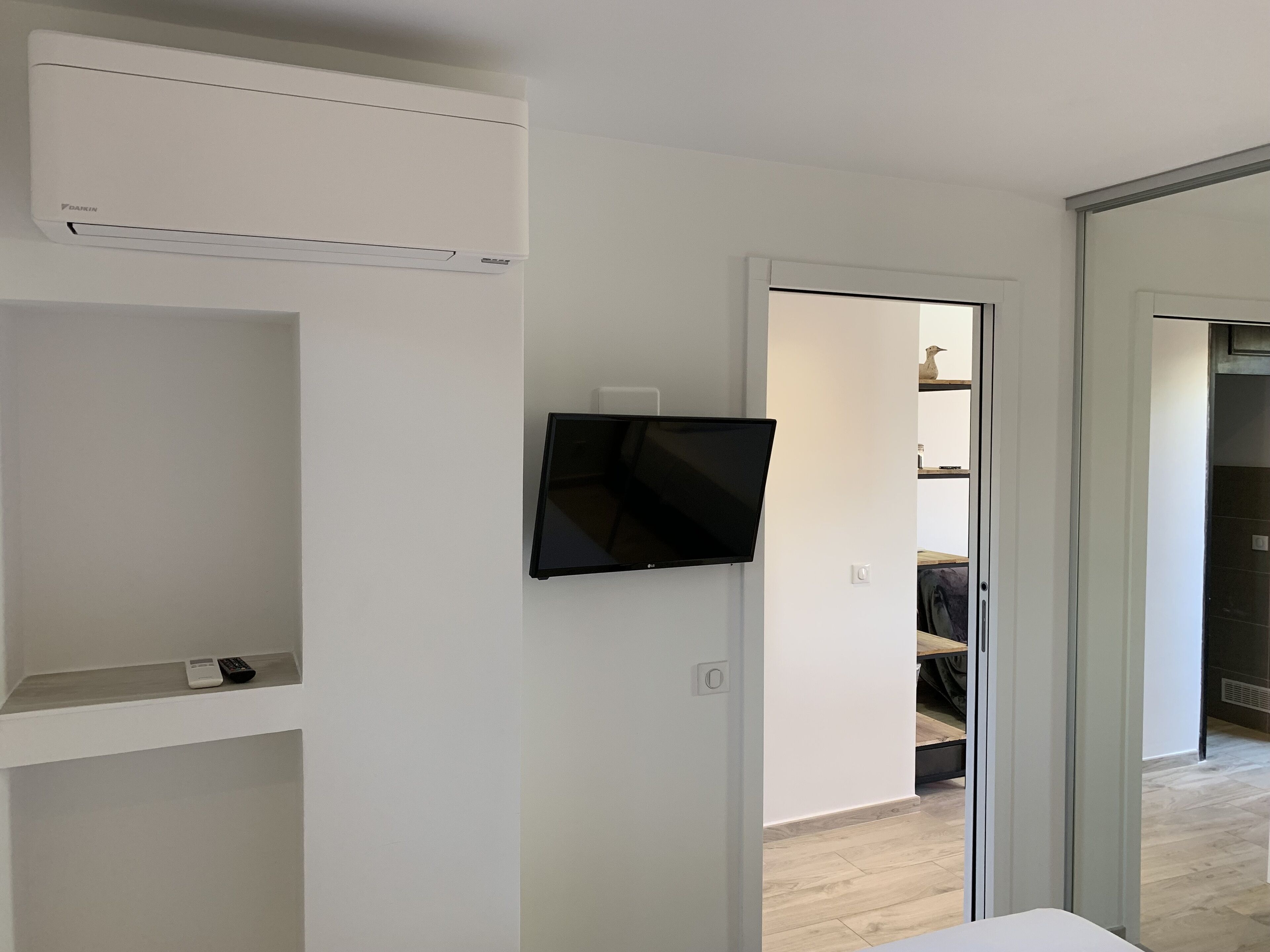 A modern room with a mounted TV, white walls, and a wooden floor.