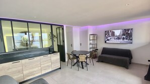 Una sala moderna con sofá, mesa de comedor con sillas, zona de cocina con fregadero y estantería.