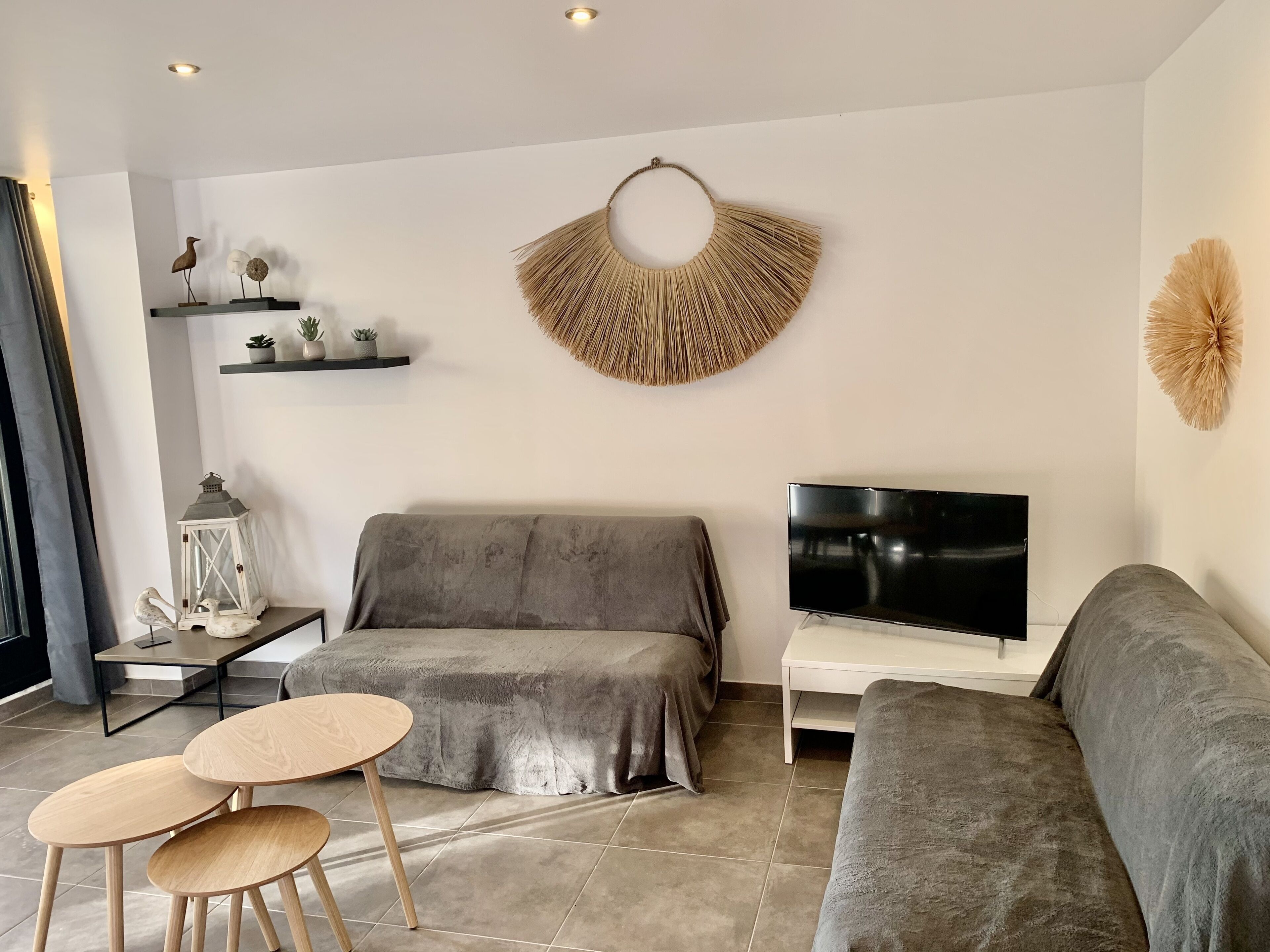 A modern living room with a grey sofa, a TV, and a decorative wall hanging.
