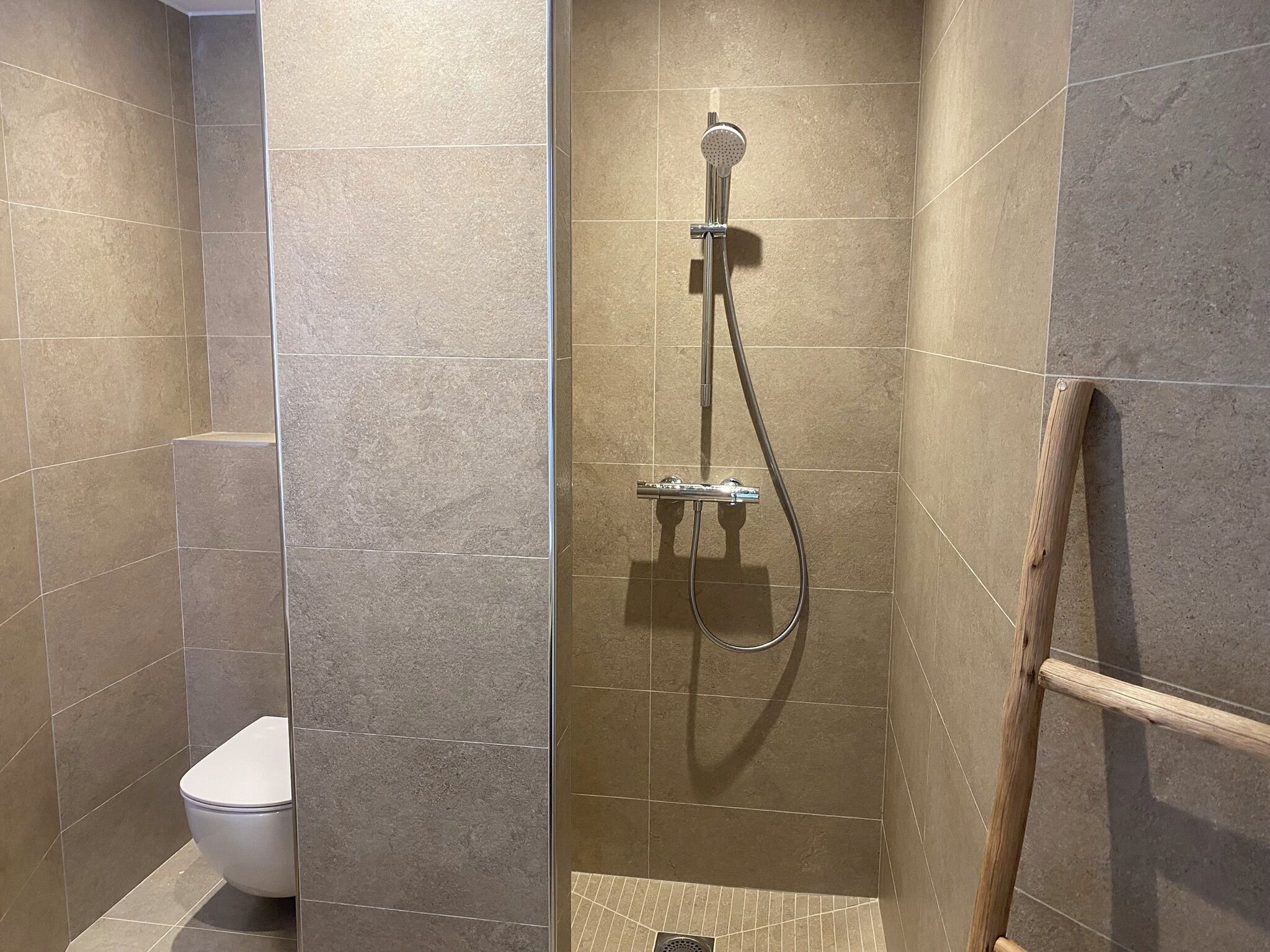 Ein modernes Badezimmer mit Dusche, Toilette und einer Holzleiter für die Badewanne.