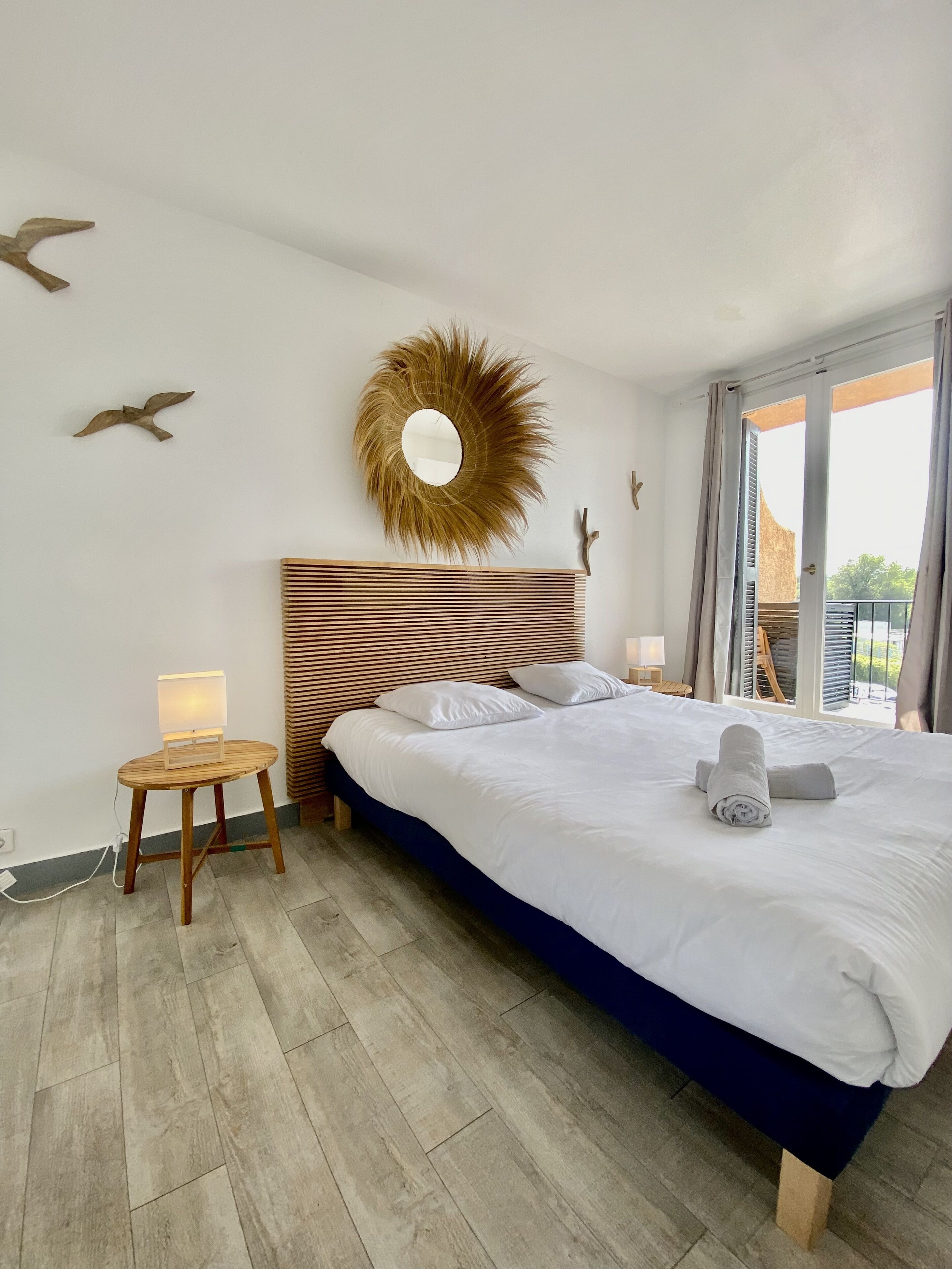 Een slaapkamer met een groot bed, een ronde spiegel en een klein tafeltje.