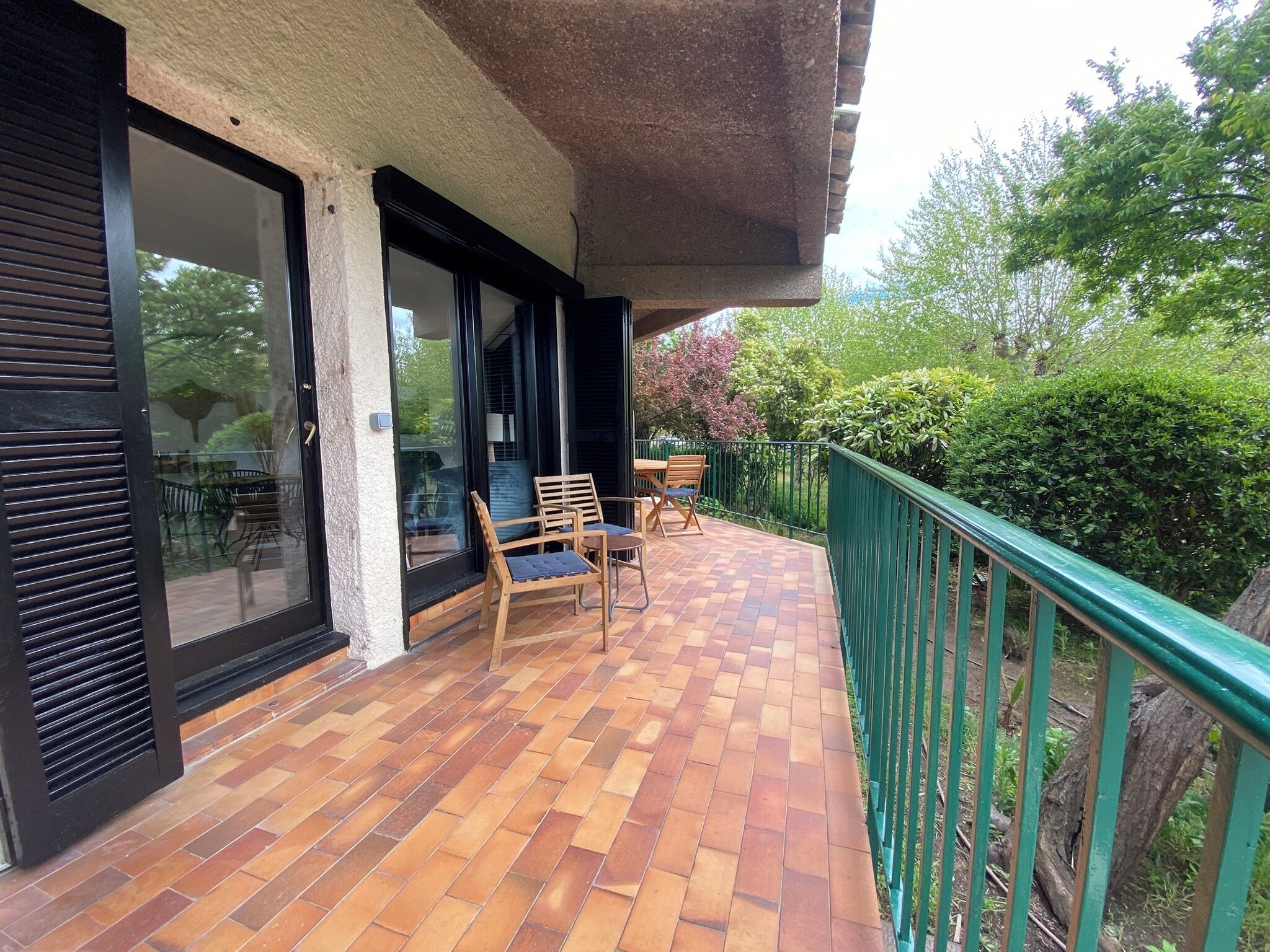 A covered outdoor area with a tiled floor, wooden chairs, and a green railing.