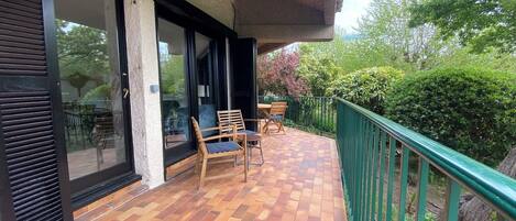 A covered outdoor area with a tiled floor, wooden chairs, and a green railing.