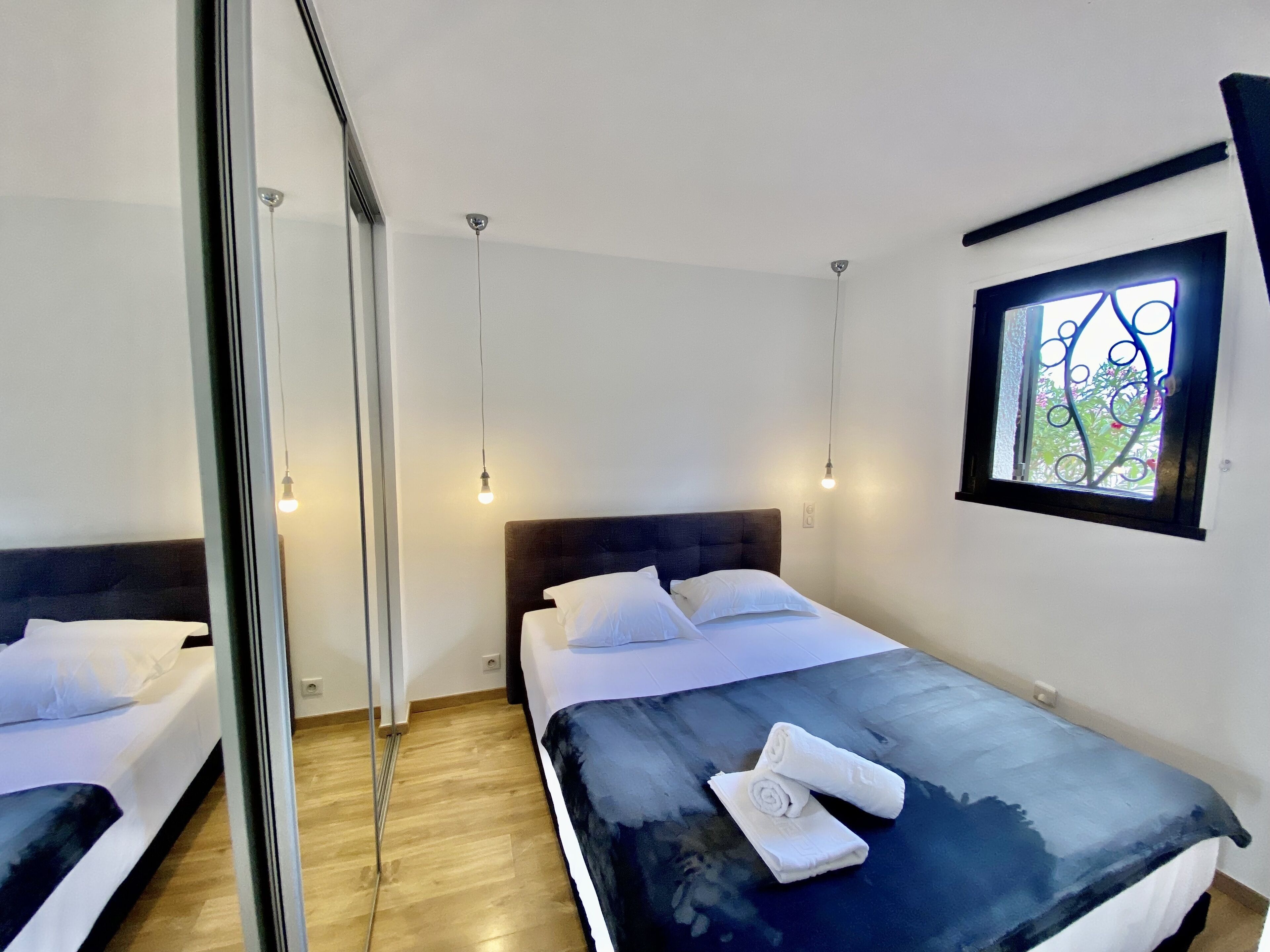 A modern hotel room with a large bed, a window with decorative ironwork, and a view of greenery outside.