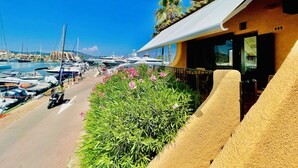 Un puerto deportivo con barcos amarrados, una carretera con una motocicleta y un edificio con balcón con vistas al puerto.