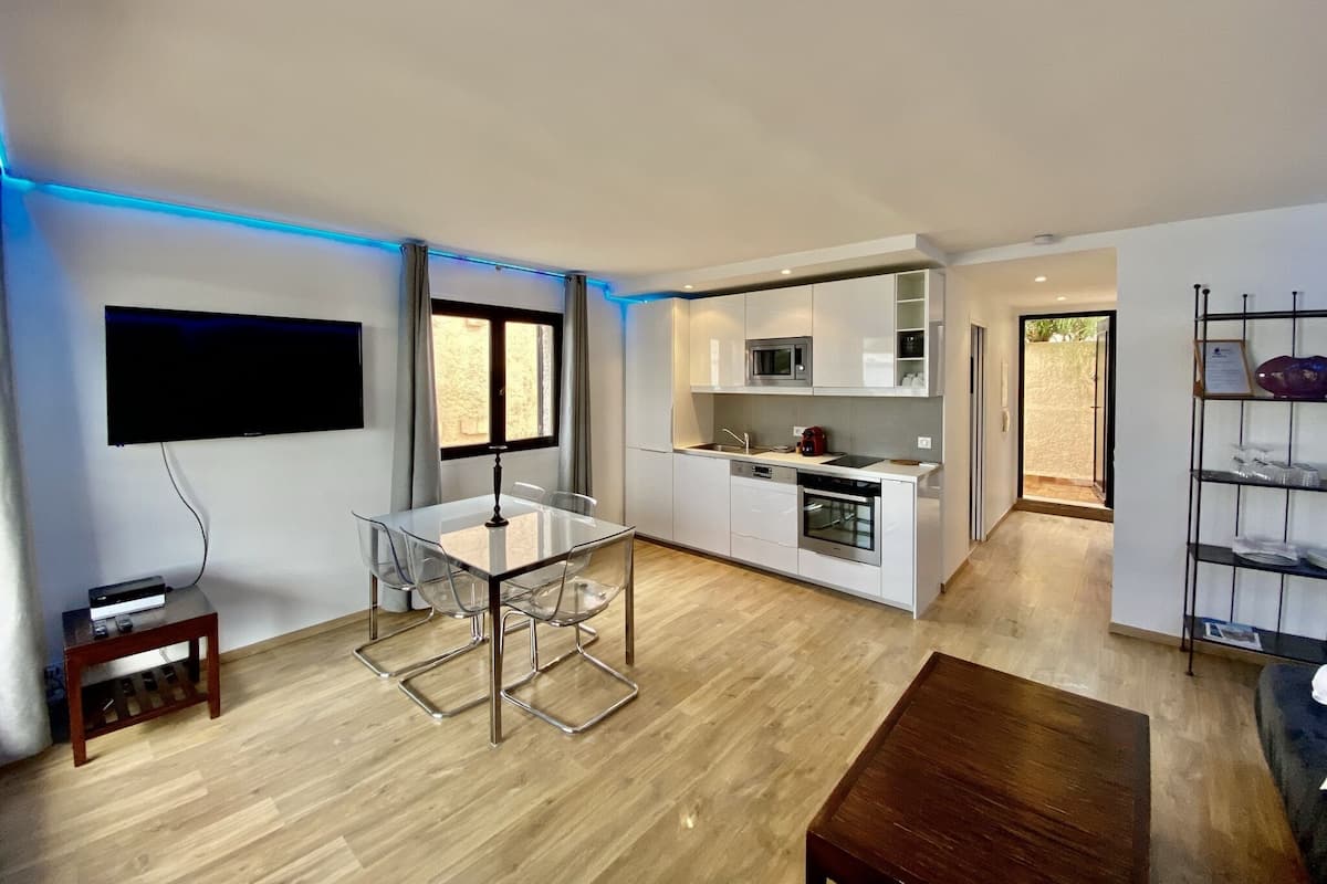 A modern kitchen with white cabinets, a microwave, and a dishwasher. There is a dining area with a glass table and chairs.