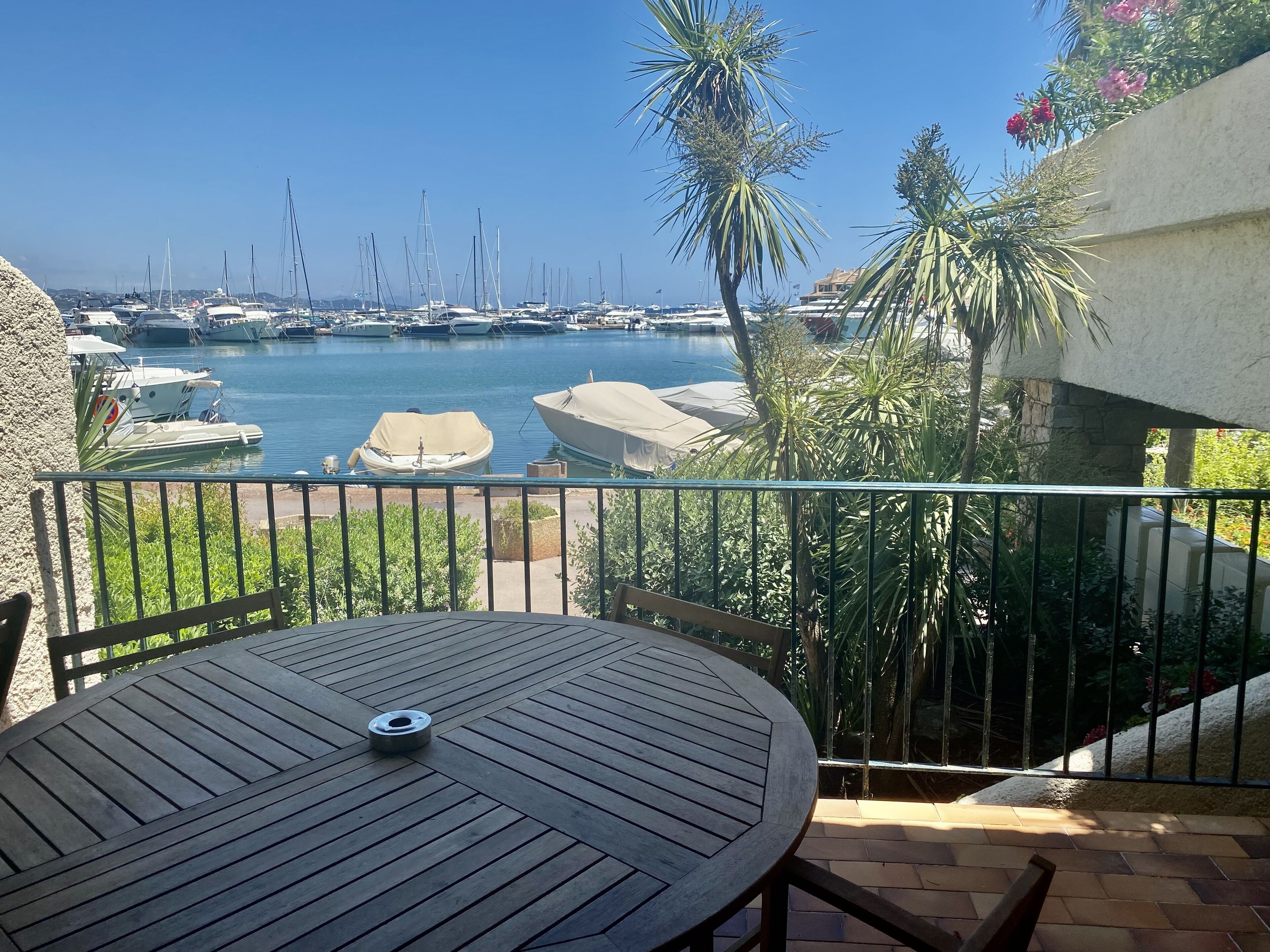 Een balkon met uitzicht op een jachthaven, een ronde tafel en bloempotten.