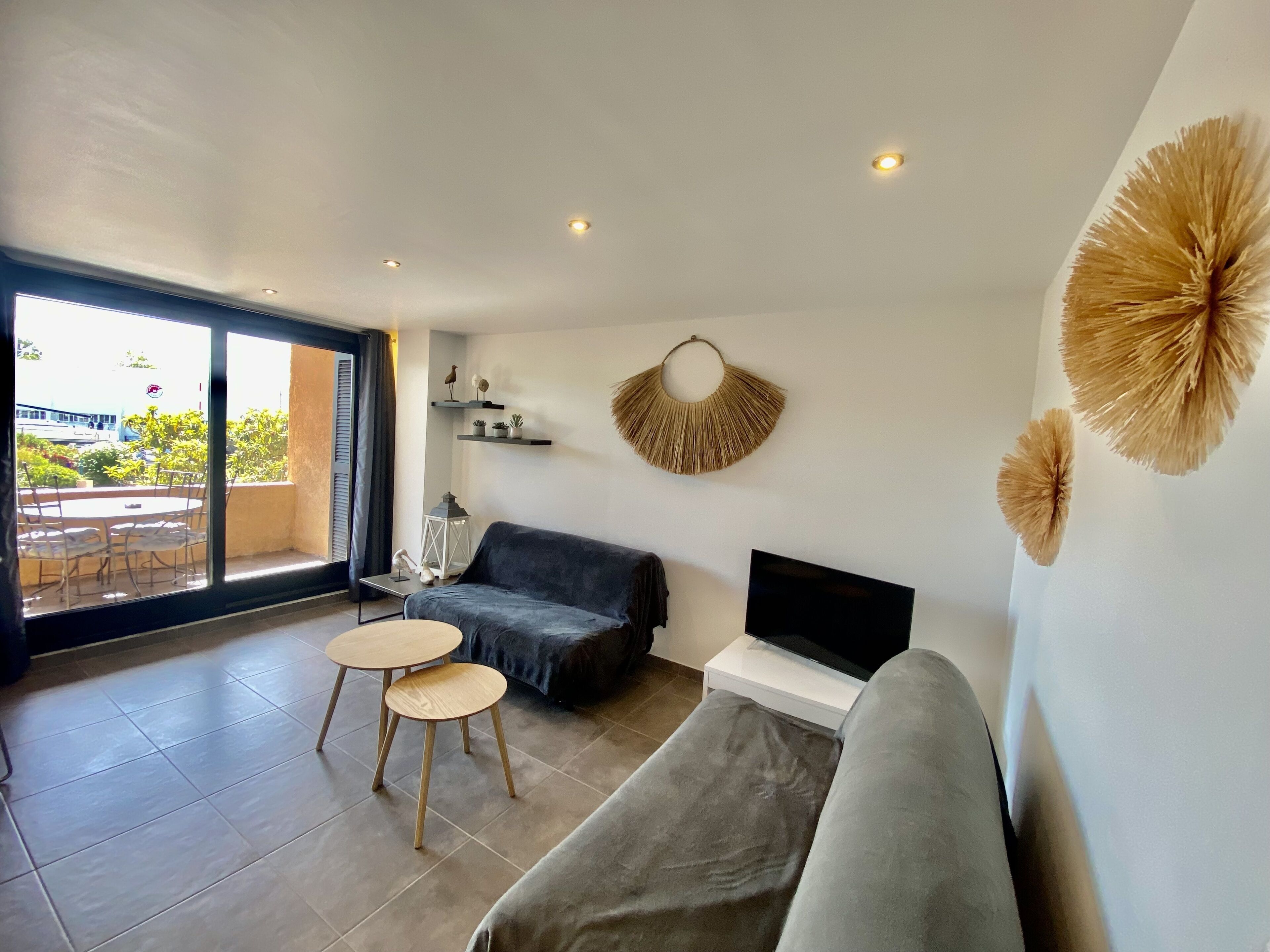 Una sala de estar moderna con un sofá gris, un televisor y una zona de comedor con sillas y una mesa.