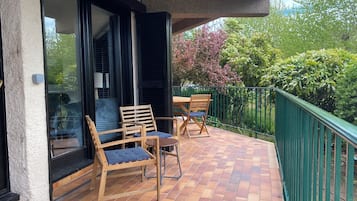 Un balcón con mesa y sillas de madera, una puerta de cristal y barandilla verde.