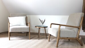 Ein Zimmer mit zwei Stühlen und einem kleinen Tisch, einem Teppich auf dem Boden und einer schlichten Wand.