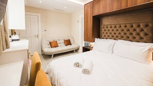 Habitación de hotel con una cama grande, cabecero de madera, sofá, escritorio y espejo.