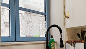 Una cocina con un lavabo negro, una ventana con cortinas de encaje y una botella de detergente para platos verde.