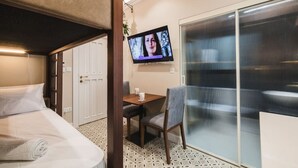 A compact hotel room with a bunk bed, a small desk with a chair, a television, and a sliding glass door leading to a balcony. - Zebbuga guest house Malta 5 (Ħaż-Żebbuġ)