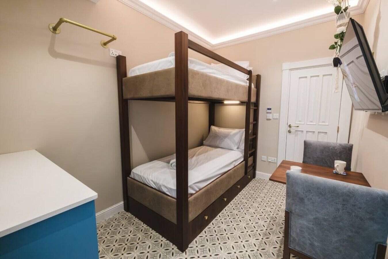 A bunk bed room with a desk and chair, a small table with a cup, and a TV mounted on the wall.