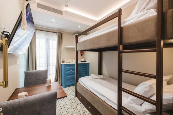 Habitació d'hotel amb literes, una taula de treball amb cadira, un televisor fixat a la paret i un armari.