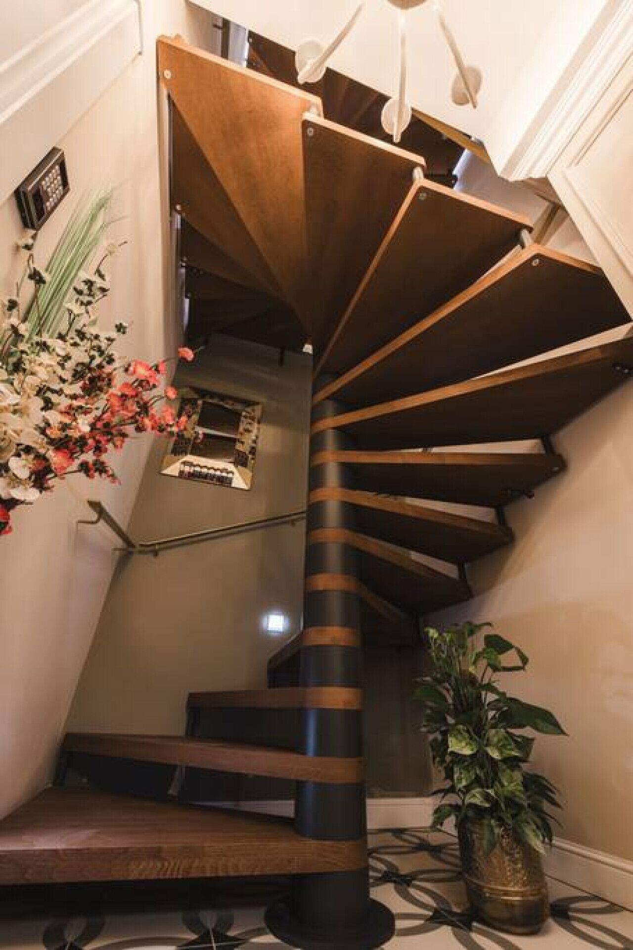 A spiral staircase with wooden steps and a black handrail, leading to an upper floor.