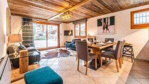 A cozy living room with a wooden ceiling, a dining area with a wooden table and chairs, a large window, and a TV mounted on the wall. - 250m from ski lifts, Ground floor, terrace, parking, tv, ski locker, 58m², Morzine (Morzine)