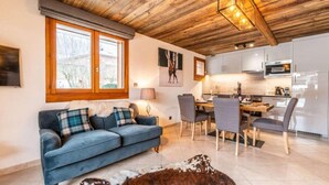 A modern living room with a blue sofa, dining table, and chairs. There is a kitchen area with cabinets and appliances. - 250m from ski lifts, Ground floor, terrace, parking, tv, ski locker, 58m², Morzine (Morzine)