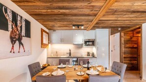 A dining area with a wooden table set for four, grey upholstered chairs, and a kitchen in the background. - 250m from ski lifts, Ground floor, terrace, parking, tv, ski locker, 58m², Morzine (Morzine)